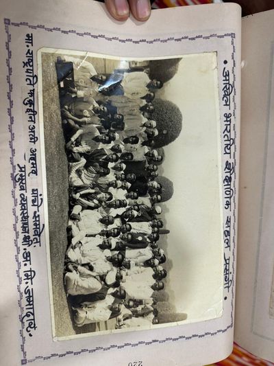 A large group/assembly photograph from an educational gathering, pasted sideways on the album page; the handwritten caption is rotated and partly illegible, so exact event details could not be confirmed with confidence.