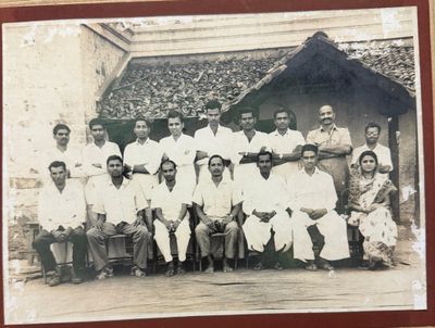 An old, undated group photograph believed to show school staff and colleagues outside a tiled-roof building.